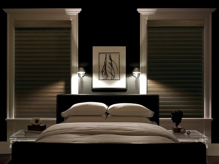 Dark bedroom with shades drawn and two bedside lamps on.